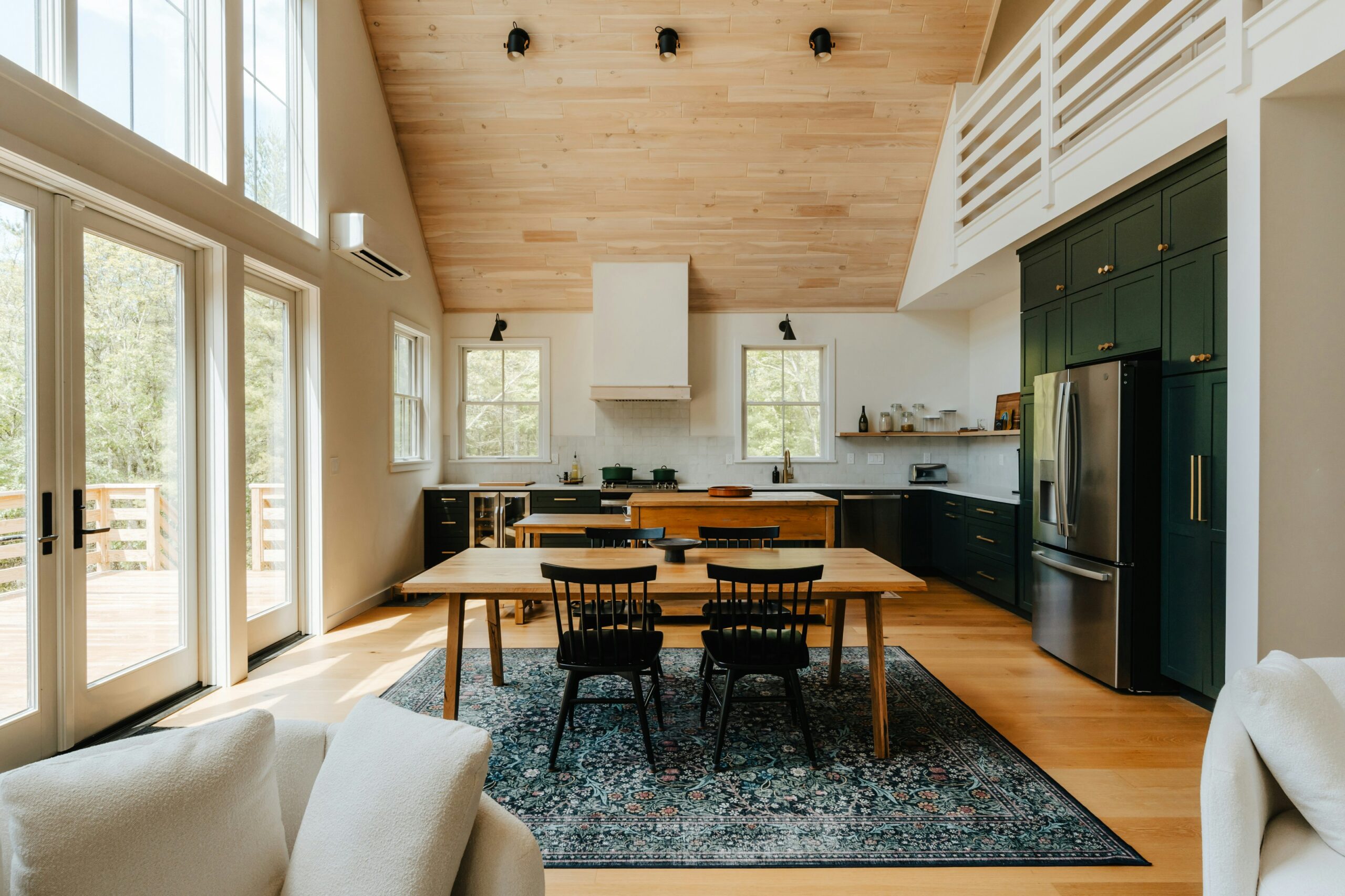 Grande cuisine ferme moderne avec plafond en bois clair, îlot en bois, armoires vert foncé et portes-fenêtres lumineuses.