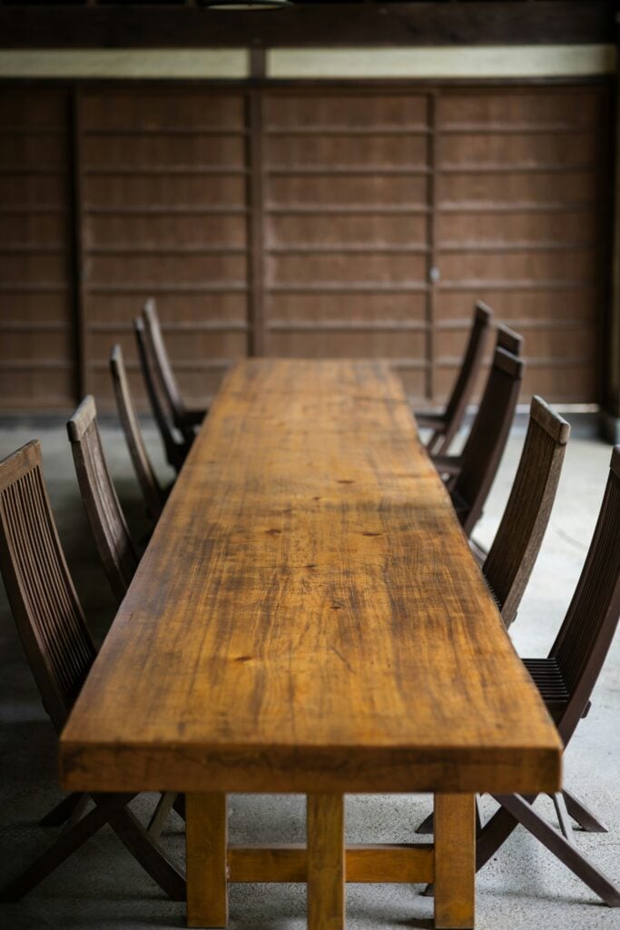 Très longue table de salle à manger en bois massif rustique, entourée de chaises pliantes en bois de teck.