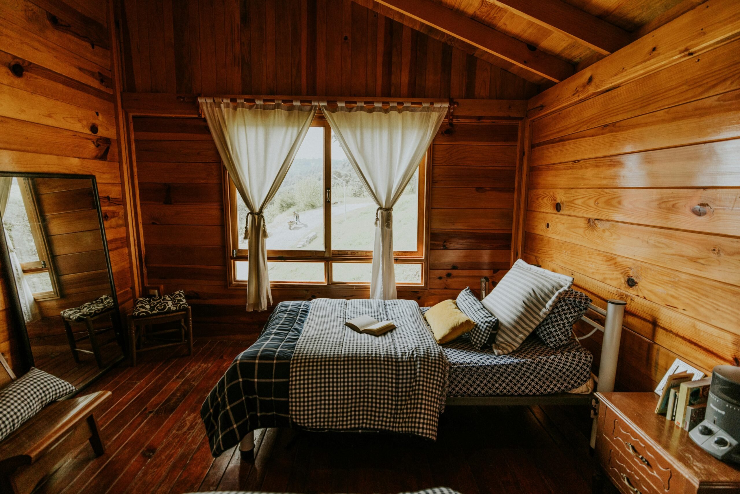 Chambre rustique en bois dans un chalet avec lit et fenêtre donnant sur la nature