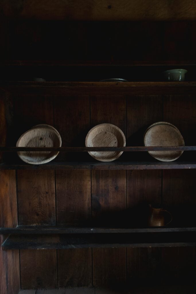 Détail d'une étagère ancienne en bois très sombre affichant trois bols ou assiettes en bois brut.